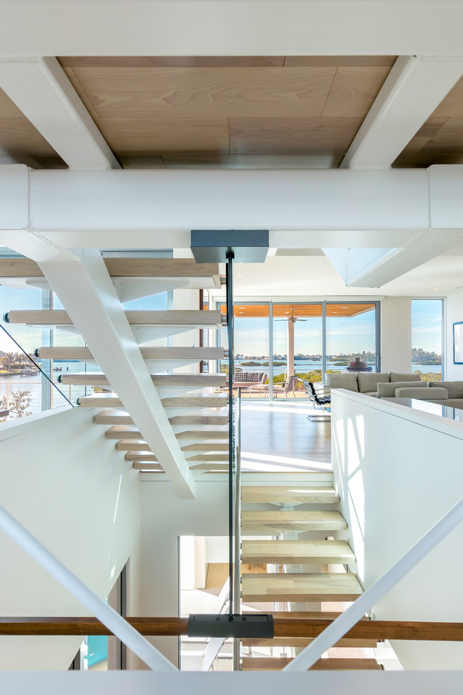 Стильный дизайн: огромная лестница на больцах в современном стиле с деревянными ступенями и стеклянными перилами без подступенок - последний тренд