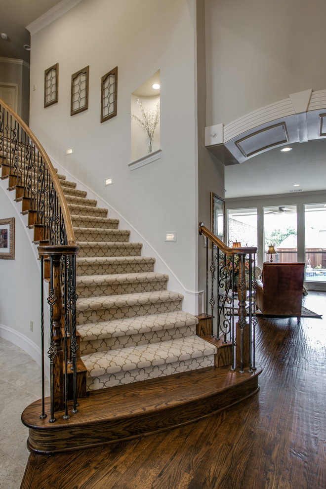 Пример оригинального дизайна: большая изогнутая металлическая лестница в классическом стиле с ступенями с ковровым покрытием и металлическими перилами