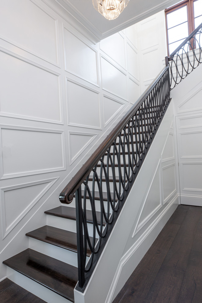 На фото: огромная угловая лестница в классическом стиле с деревянными ступенями, крашенными деревянными подступенками и металлическими перилами с