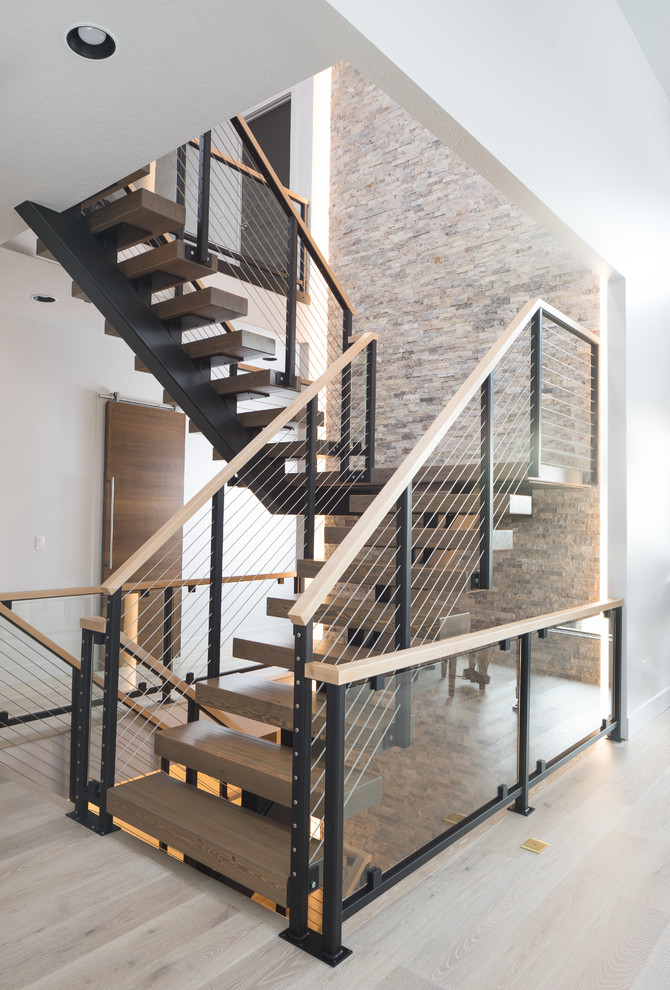 На фото: большая металлическая лестница на больцах в современном стиле с деревянными ступенями и перилами из тросов с