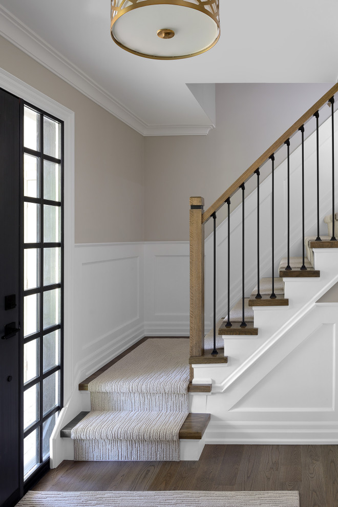 На фото: угловая лестница среднего размера в стиле неоклассика (современная классика) с ступенями с ковровым покрытием, крашенными деревянными подступенками, перилами из смешанных материалов и панелями на стенах с