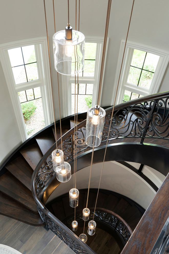 На фото: большая изогнутая деревянная лестница в классическом стиле с деревянными ступенями и металлическими перилами с