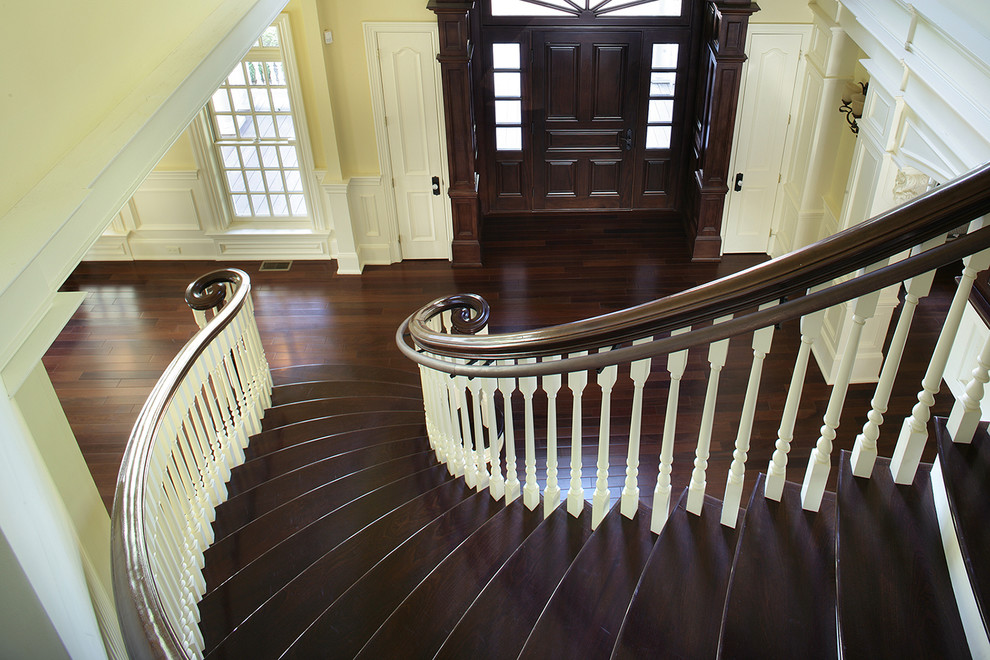 This is an example of a large classic wood curved staircase in New York with wood risers.