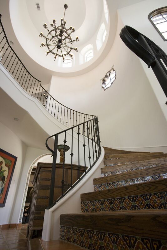 На фото: большая изогнутая лестница в средиземноморском стиле с деревянными ступенями, подступенками из плитки и металлическими перилами с