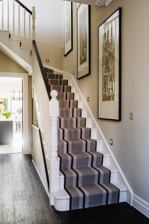 whait stairs with black and brown running and dark wood floors and three pieces of large art on the wall