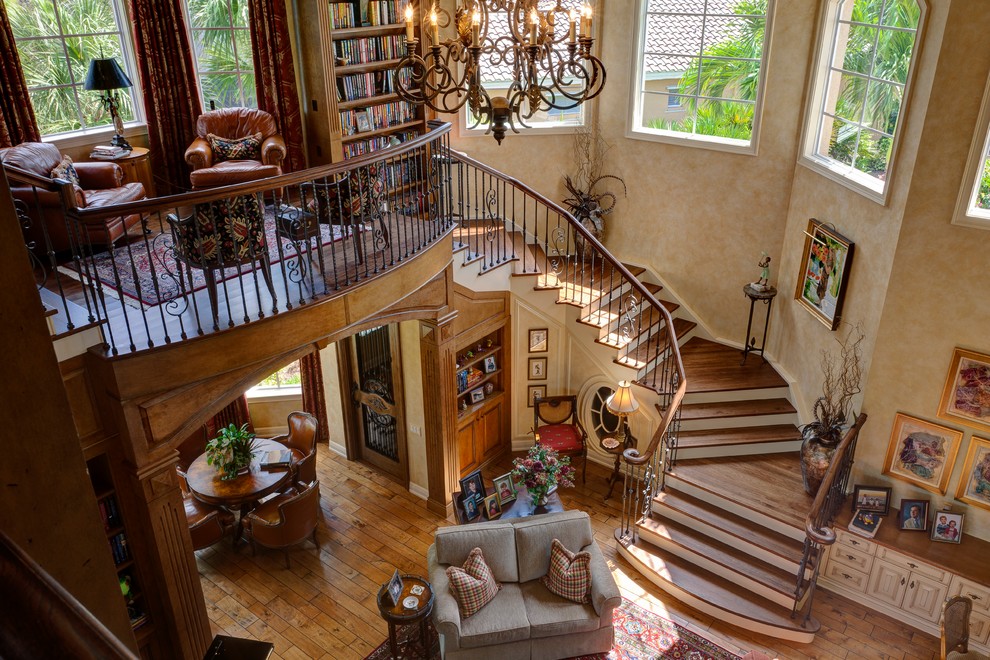 Пример оригинального дизайна: большая изогнутая лестница в классическом стиле с деревянными ступенями, крашенными деревянными подступенками и металлическими перилами