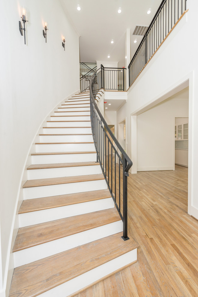 На фото: изогнутая лестница среднего размера в стиле неоклассика (современная классика) с деревянными ступенями, крашенными деревянными подступенками и металлическими перилами с