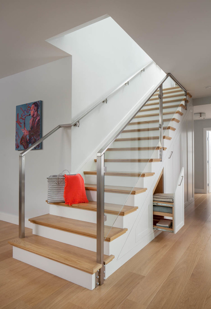 Стильный дизайн: прямая лестница в стиле неоклассика (современная классика) с деревянными ступенями, крашенными деревянными подступенками, стеклянными перилами и кладовкой или шкафом под ней - последний тренд