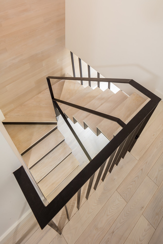 Cette image montre un grand escalier design en U avec des marches en bois, des contremarches en métal et un garde-corps en métal.