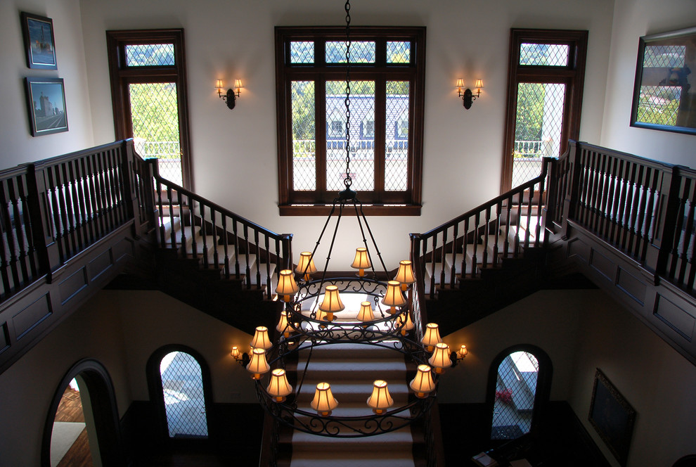 Пример оригинального дизайна: огромная изогнутая лестница в викторианском стиле с ступенями с ковровым покрытием и ковровыми подступенками
