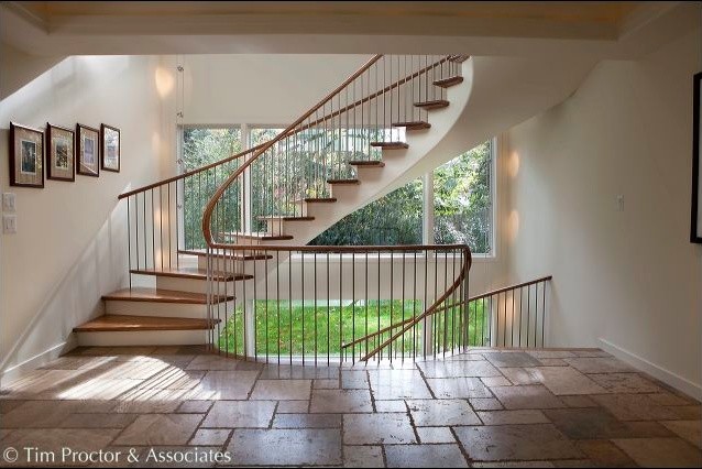 На фото: большая изогнутая деревянная лестница в современном стиле с деревянными ступенями и металлическими перилами с