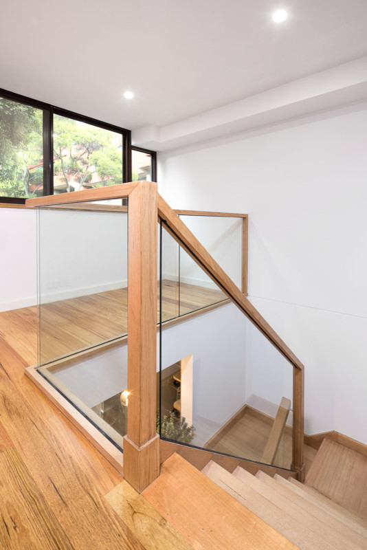 Cette image montre un petit escalier courbe bohème avec des marches en bois, des contremarches en verre et un garde-corps en bois.