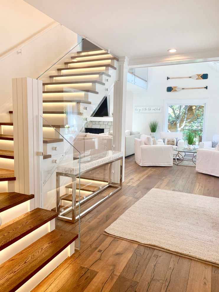 Свежая идея для дизайна: огромная угловая лестница в современном стиле с деревянными ступенями, крашенными деревянными подступенками и стеклянными перилами - отличное фото интерьера