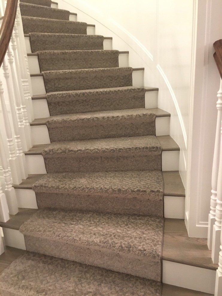 Пример оригинального дизайна: огромная изогнутая лестница в классическом стиле с ступенями с ковровым покрытием, ковровыми подступенками и деревянными перилами