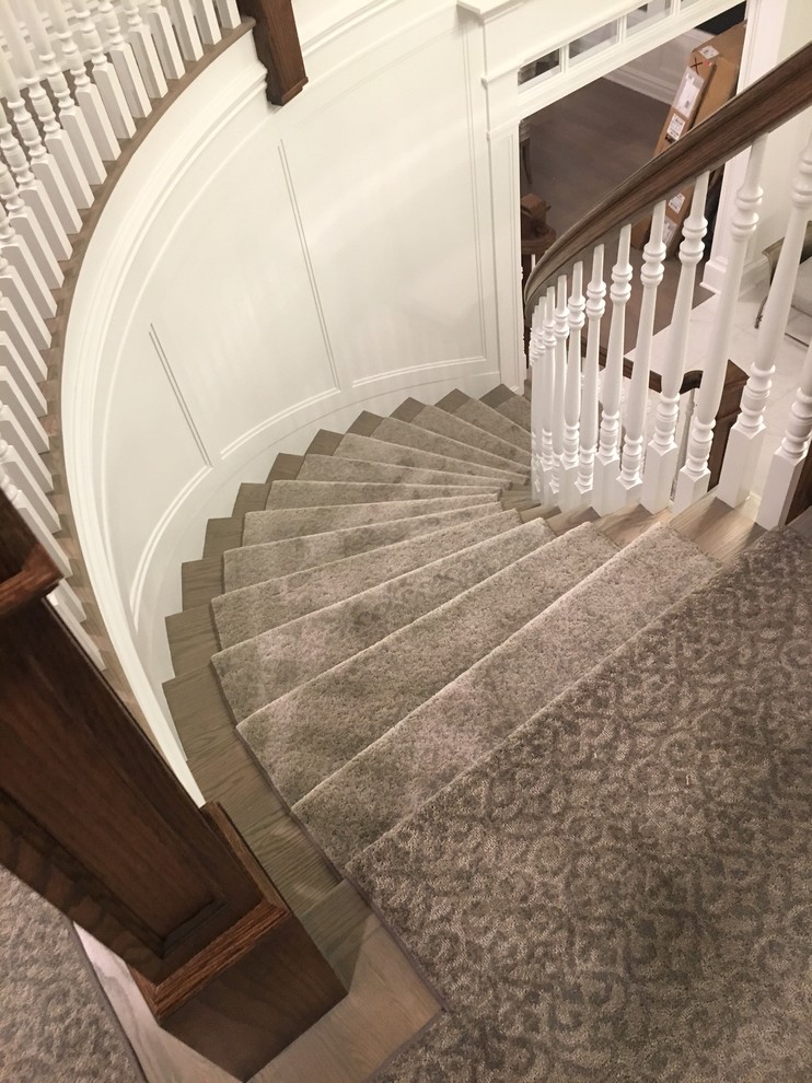 На фото: огромная изогнутая лестница в классическом стиле с ступенями с ковровым покрытием, ковровыми подступенками и деревянными перилами