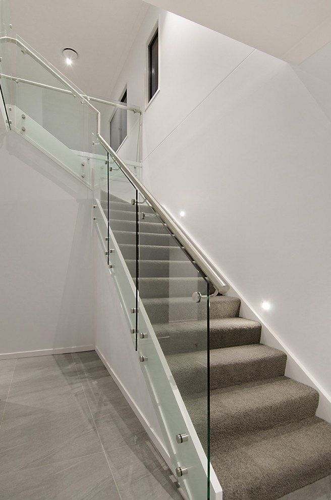 Cette photo montre un escalier moderne en L de taille moyenne avec des marches en moquette, des contremarches en moquette et un garde-corps en verre.