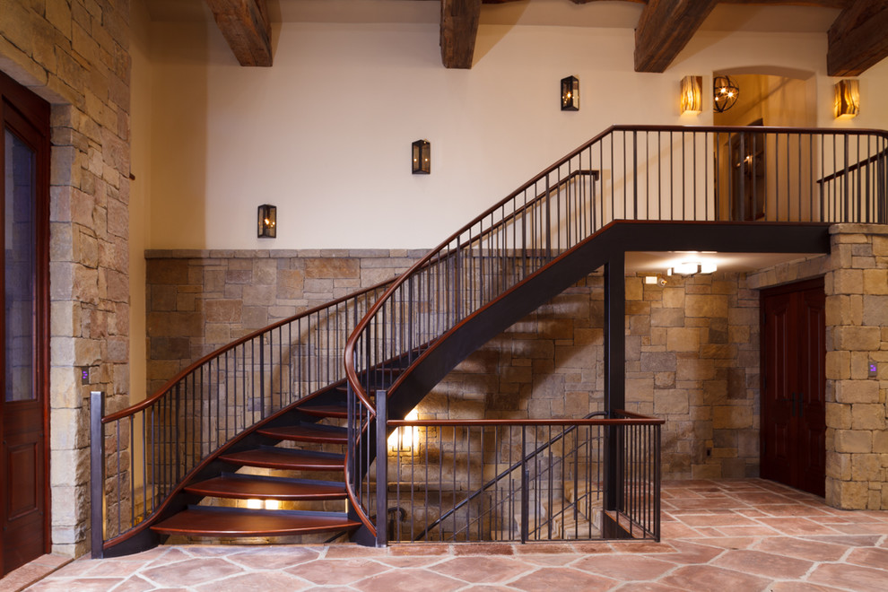 На фото: большая изогнутая лестница в средиземноморском стиле с деревянными ступенями и металлическими перилами без подступенок