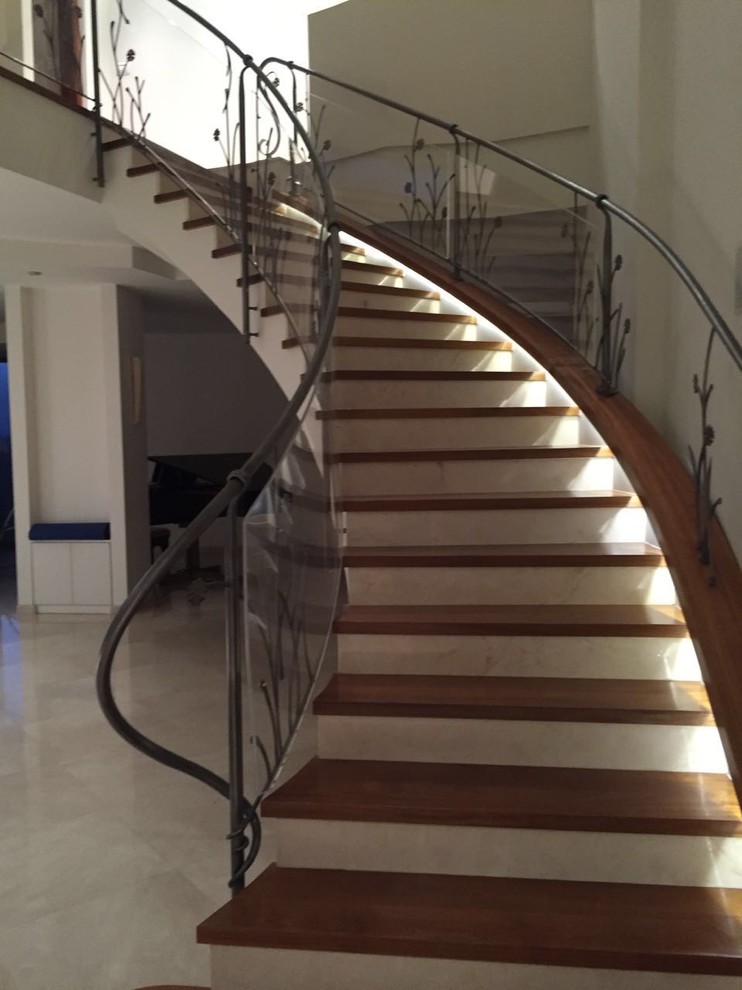 Imagen de escalera curva contemporánea con escalones de madera y contrahuellas de vidrio