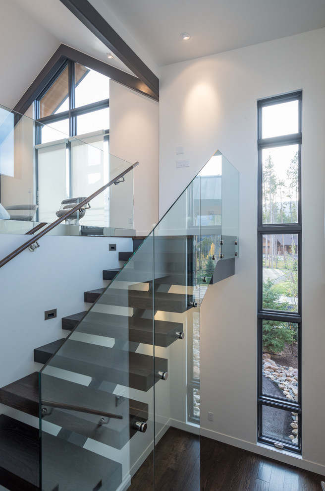 Пример оригинального дизайна: большая лестница на больцах в стиле модернизм с деревянными ступенями и стеклянными перилами без подступенок