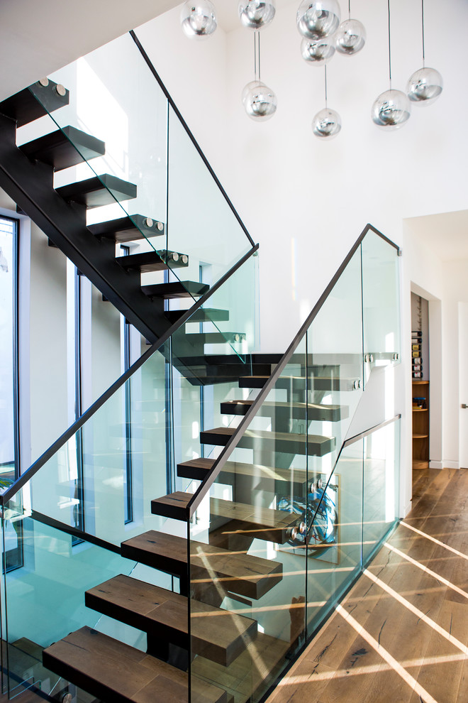 Cette photo montre un grand escalier flottant tendance avec des marches en bois, un garde-corps en verre et éclairage.