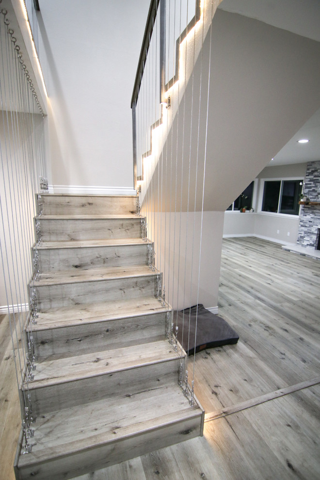 На фото: п-образная деревянная лестница среднего размера в стиле модернизм с деревянными ступенями и перилами из тросов с