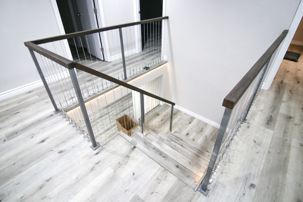 Cette image montre un escalier minimaliste en U de taille moyenne avec des marches en bois, des contremarches en bois et un garde-corps en câble.
