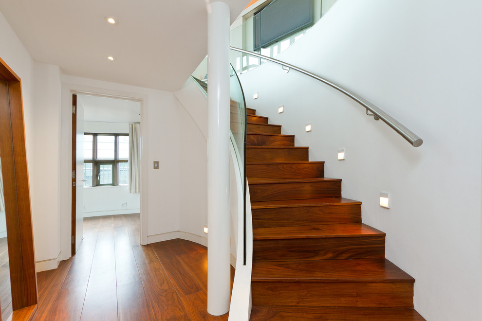 Diseño de escalera curva actual con escalones de madera, contrahuellas de madera y barandilla de vidrio