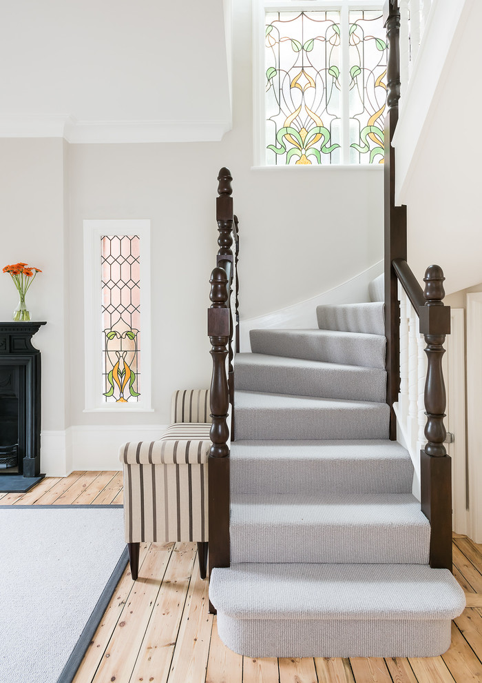 На фото: изогнутая лестница в викторианском стиле с ступенями с ковровым покрытием, ковровыми подступенками и деревянными перилами с