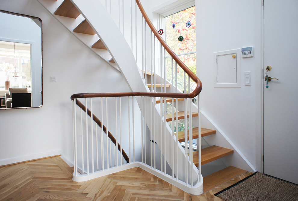 На фото: изогнутая деревянная лестница в стиле неоклассика (современная классика) с деревянными ступенями и деревянными перилами с
