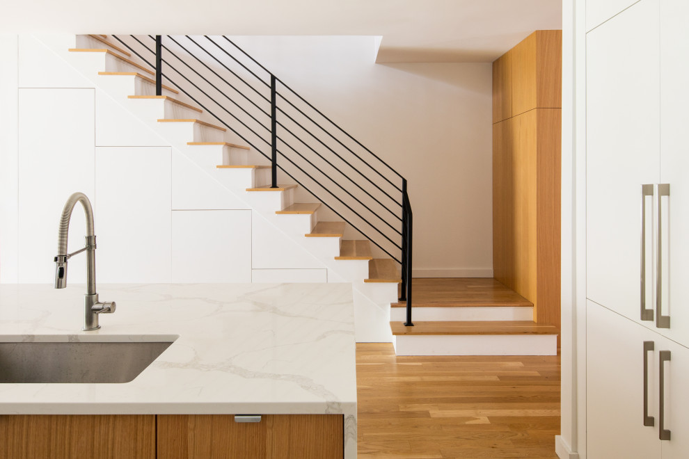 This is an example of a medium sized modern wood l-shaped metal railing staircase in New York with painted wood risers.