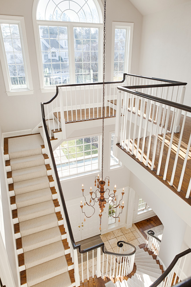 Exempel på en mycket stor klassisk svängd trappa, med heltäckningsmatta, sättsteg med heltäckningsmatta och räcke i trä