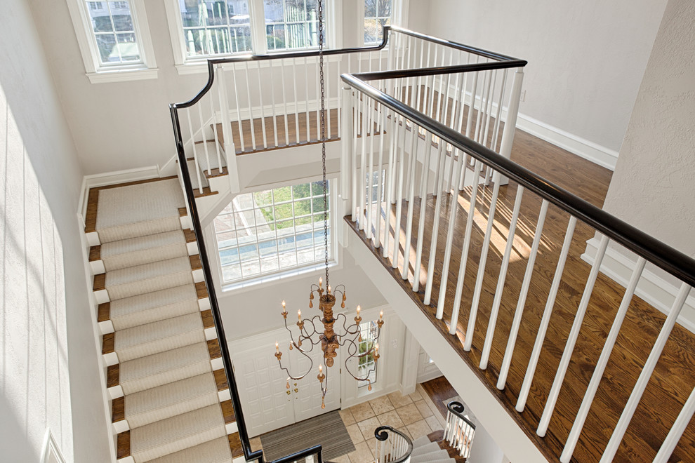 Идея дизайна: огромная изогнутая лестница в классическом стиле с ступенями с ковровым покрытием, ковровыми подступенками и деревянными перилами