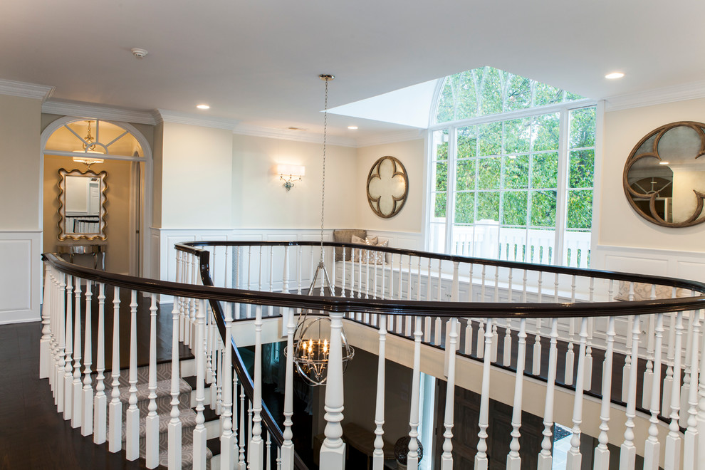 На фото: огромная изогнутая лестница в классическом стиле с ступенями с ковровым покрытием и ковровыми подступенками с