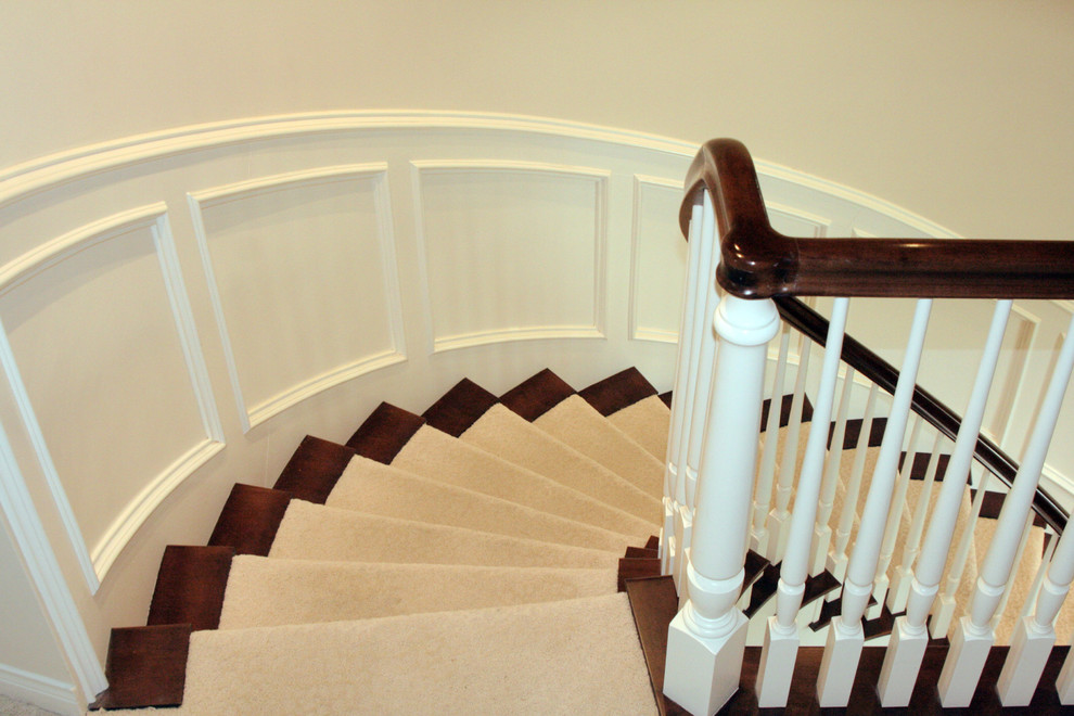 Стильный дизайн: изогнутая лестница в стиле ретро с ступенями с ковровым покрытием, ковровыми подступенками, деревянными перилами и панелями на стенах - последний тренд