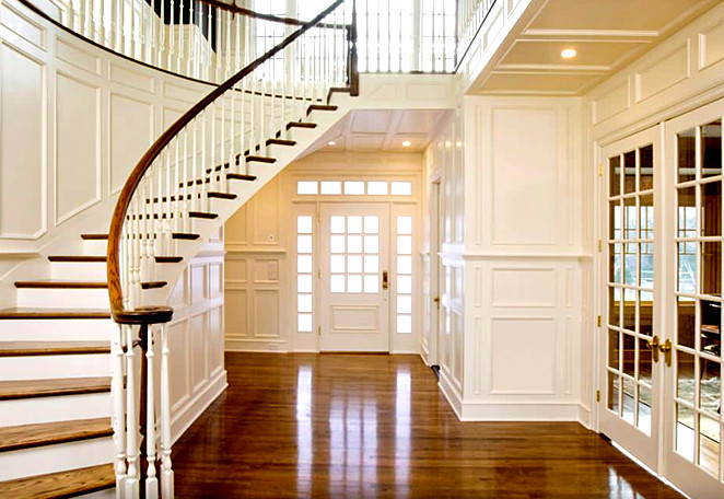 Пример оригинального дизайна: большая изогнутая лестница в классическом стиле с деревянными ступенями, крашенными деревянными подступенками и деревянными перилами