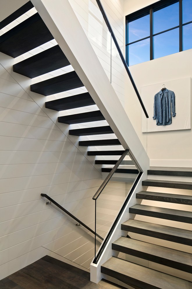 Пример оригинального дизайна: большая лестница на больцах в стиле модернизм с деревянными ступенями и стеклянными перилами без подступенок