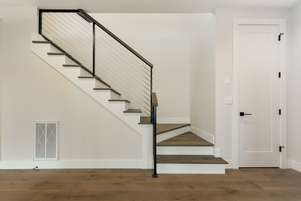 This is an example of a medium sized traditional wood l-shaped wire cable railing staircase in Seattle with painted wood risers.