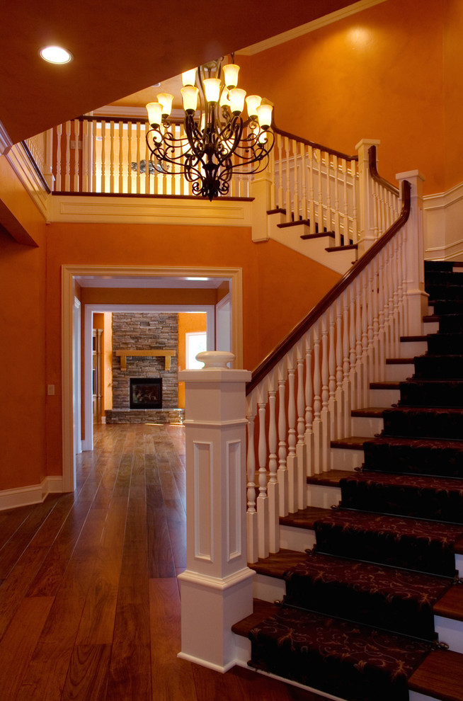 На фото: большая угловая лестница в классическом стиле с деревянными ступенями и ковровыми подступенками с