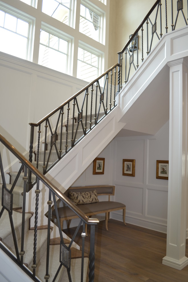 На фото: большая угловая лестница в стиле неоклассика (современная классика) с деревянными ступенями и ковровыми подступенками