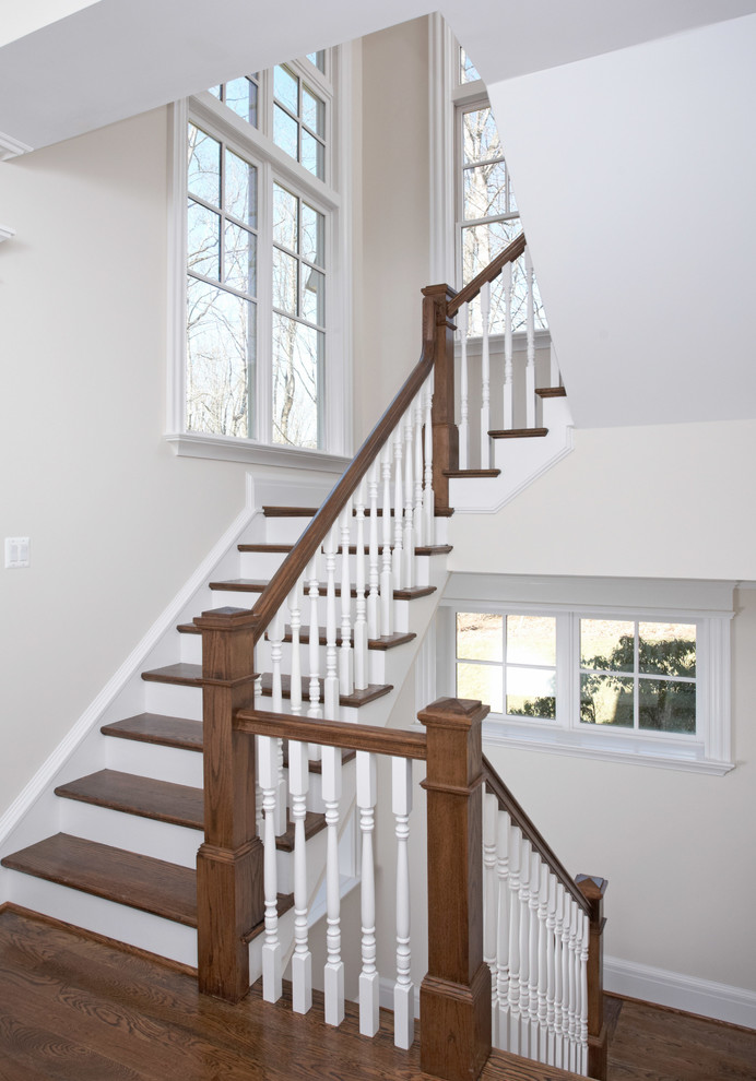 На фото: угловая лестница в классическом стиле с деревянными ступенями, крашенными деревянными подступенками и деревянными перилами с