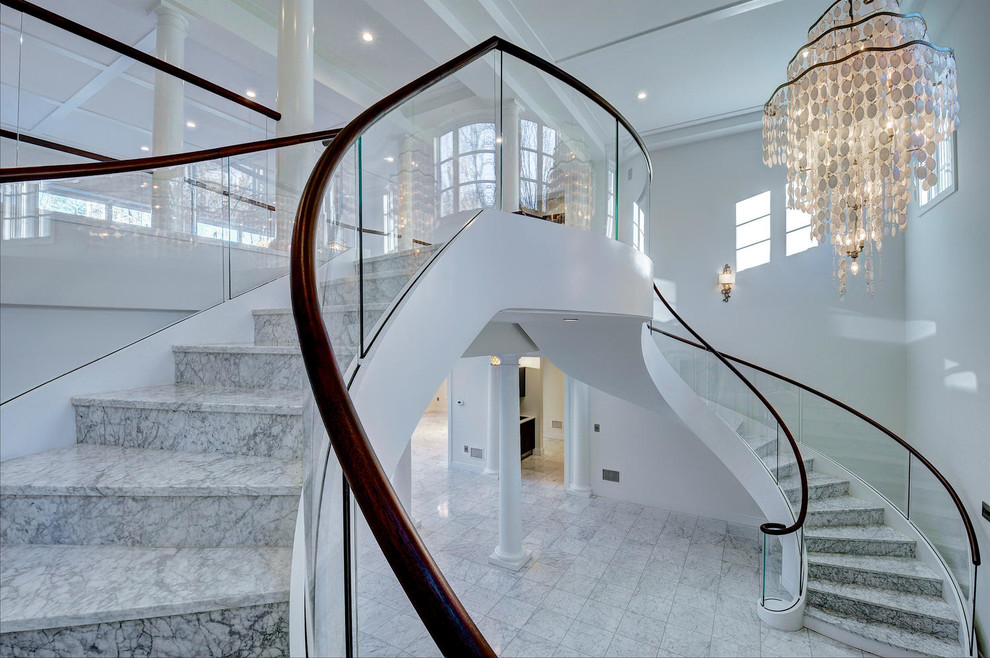 На фото: большая винтовая лестница в стиле неоклассика (современная классика) с мраморными ступенями и подступенками из мрамора с
