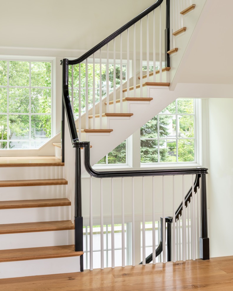 Пример оригинального дизайна: большая п-образная лестница в классическом стиле с деревянными ступенями, крашенными деревянными подступенками и деревянными перилами