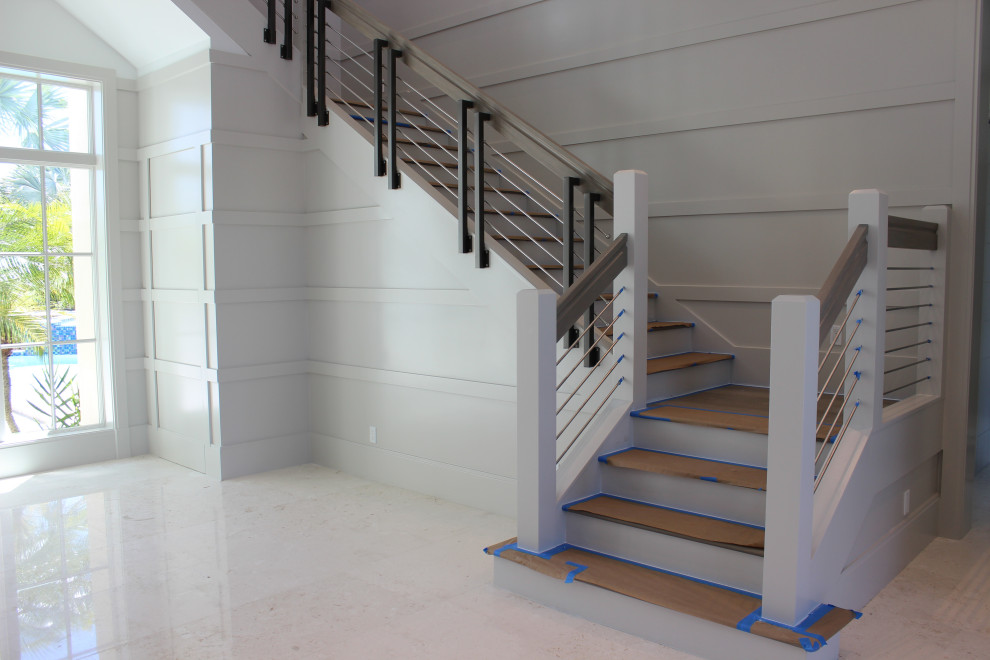 他の地域にある高級な広いトランジショナルスタイルのおしゃれなかね折れ階段 (木の蹴込み板、混合材の手すり、板張り壁) の写真