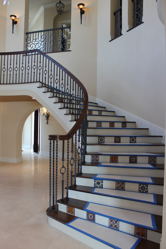 Modelo de escalera curva mediterránea grande con escalones de madera, contrahuellas con baldosas y/o azulejos y barandilla de varios materiales