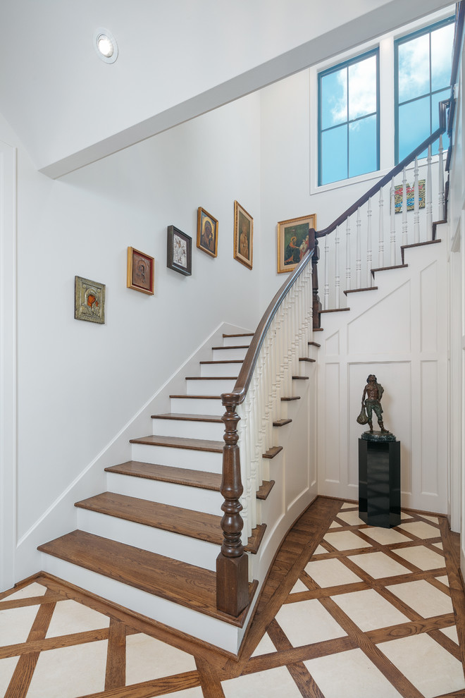 Пример оригинального дизайна: огромная п-образная лестница в стиле неоклассика (современная классика) с деревянными ступенями, деревянными перилами и крашенными деревянными подступенками