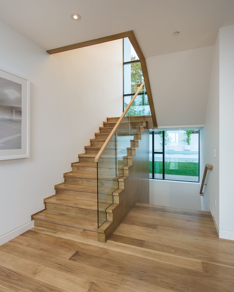Cette image montre un grand escalier design en U avec des marches en bois, des contremarches en bois et un garde-corps en verre.