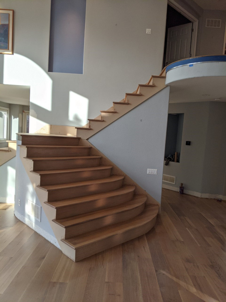 This is an example of a large contemporary curved metal railing staircase in Denver with travertine treads and wood risers.