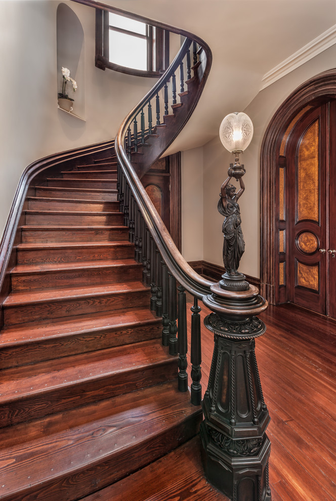 Large victorian wood curved wood railing staircase in Other with wood risers and feature lighting.