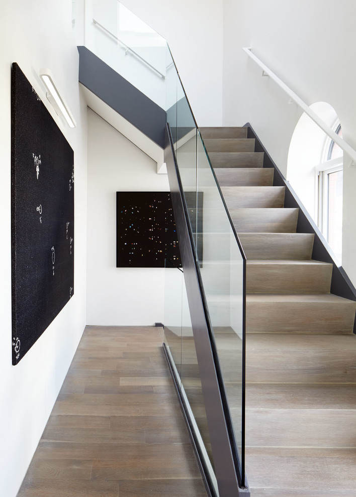 Cette image montre un grand escalier flottant minimaliste avec des marches en bois, des contremarches en bois et un garde-corps en verre.