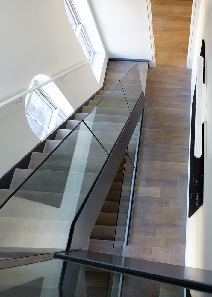 Imagen de escalera suspendida moderna grande con escalones de madera, contrahuellas de madera y barandilla de vidrio